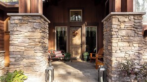 A stone-clad entrance with a wooden door, a bench, and a potted plant. - Sunriver Luxury Home at Caldera Springs - TRAI94 (Sunriver)