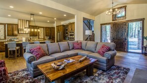 A spacious living room with a large sectional sofa, a wooden coffee table, and a kitchen in the background. - Sunriver Luxury Home at Caldera Springs - TRAI94 (Sunriver)