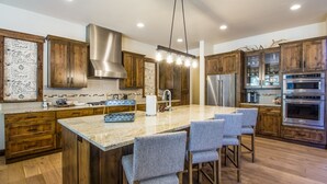 A modern kitchen with wooden cabinets, a large island with bar stools, stainless steel appliances, and a pendant light. - Sunriver Luxury Home at Caldera Springs - TRAI94 (Sunriver)