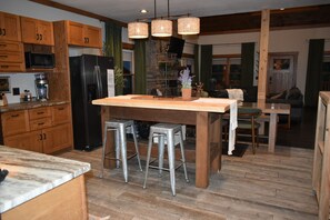 Une cuisine avec des meubles en bois, un réfrigérateur noir, un ßlot central avec des tabourets et des suspensions en osier.