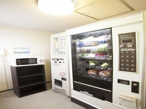 A vending machine with a microwave above it, and a small shelf unit to the left. - Business Inn Norte 2 (Sapporo)