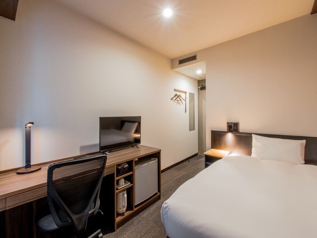 A hotel room with a bed, desk, chair, television, and a small refrigerator.