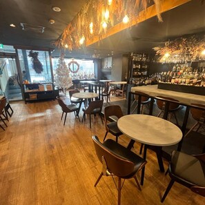 A bar area with wooden flooring, round tables, and chairs. - Business Inn Norte 2 (Sapporo)