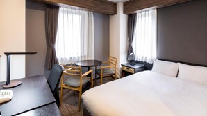 A hotel room with a bed, a desk with a telephone, a chair, a small table, and curtains. - Business Inn Norte 2 (Sapporo)