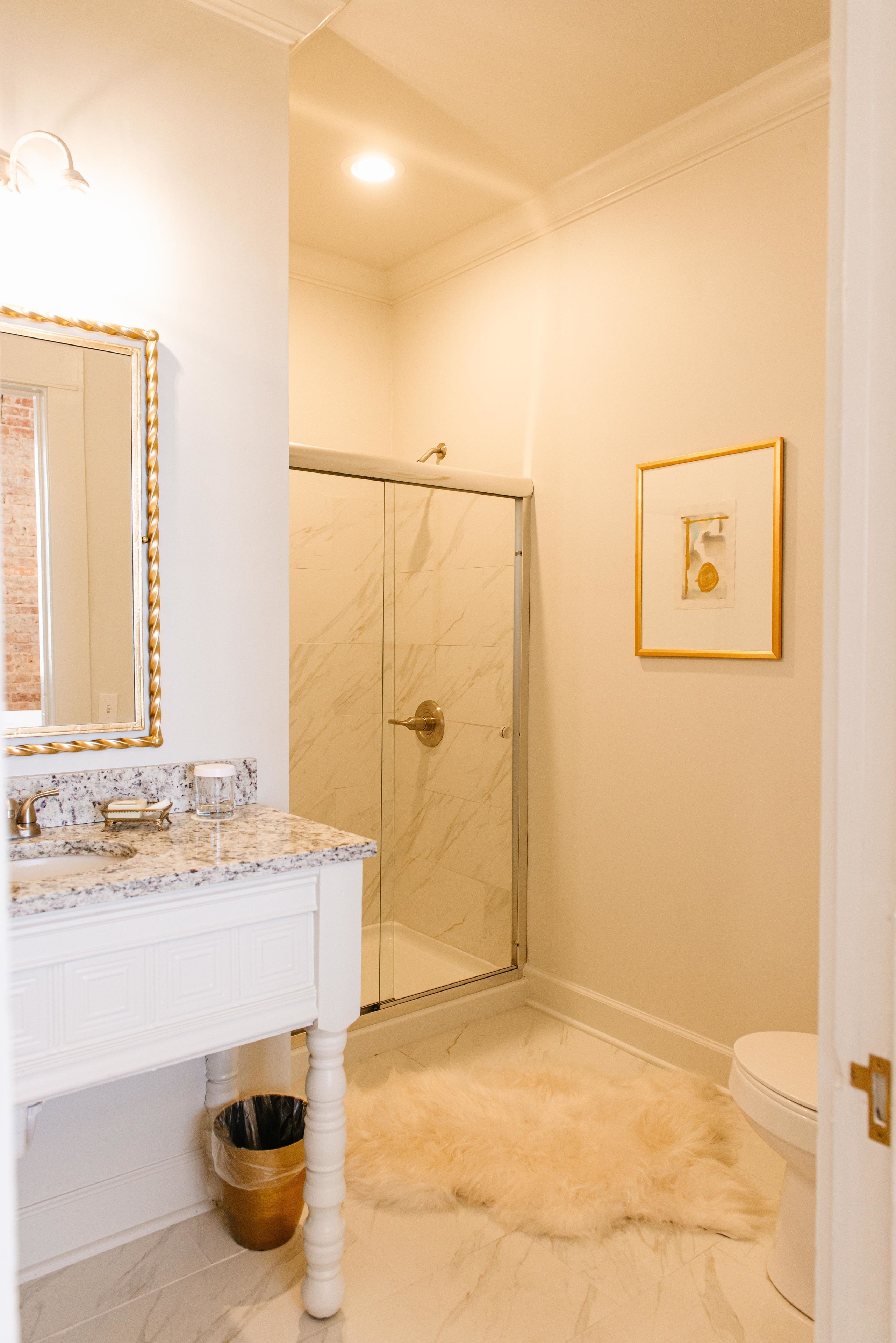 Une salle de bain avec un lavabo en marbre, une cabine de douche en verre et un tapis moelleux sur le sol.