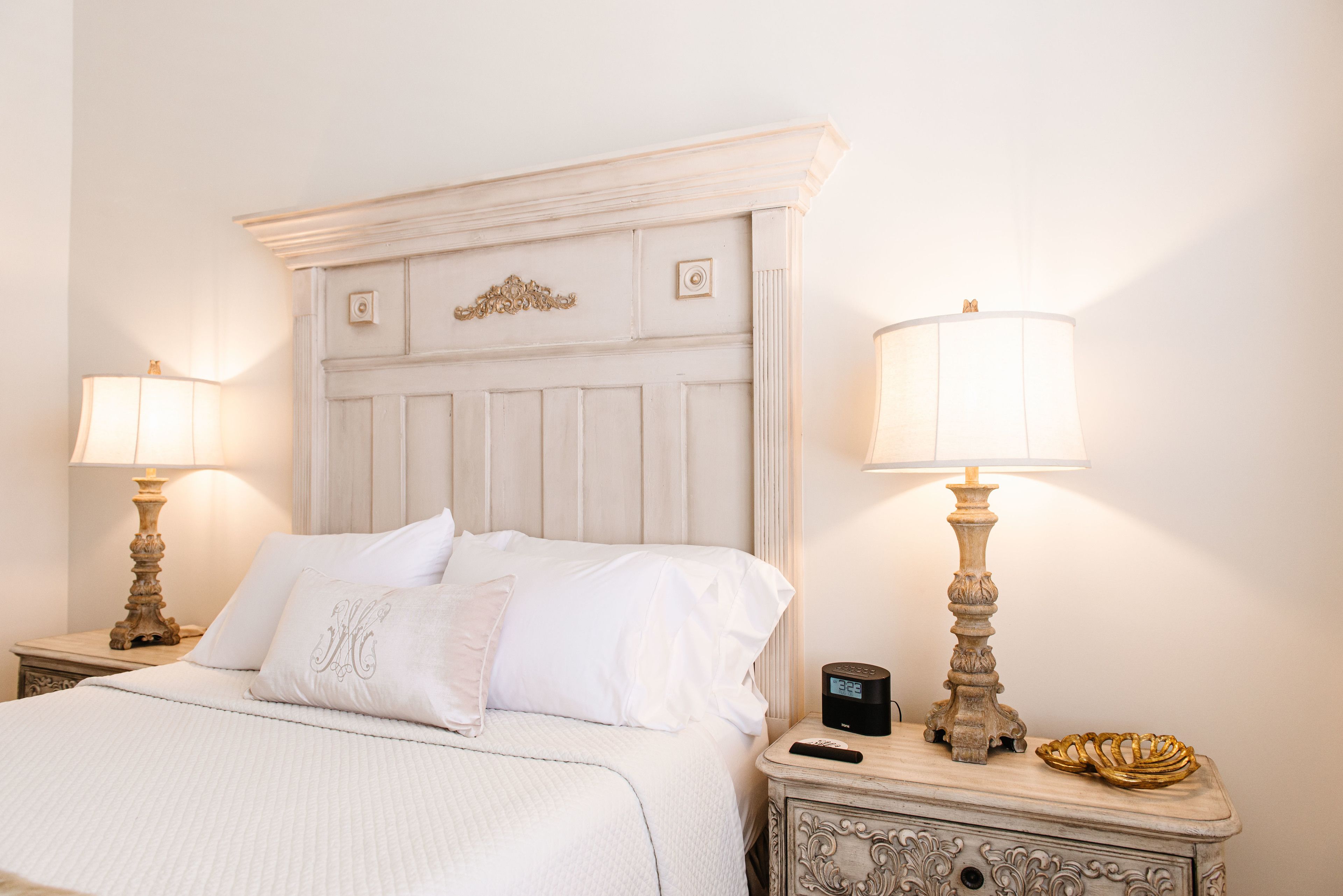 Un lit bien fait, avec du linge de lit blanc et des oreillers, flanqué de deux tables de chevet sur lesquelles reposent des lampes et une horloge.