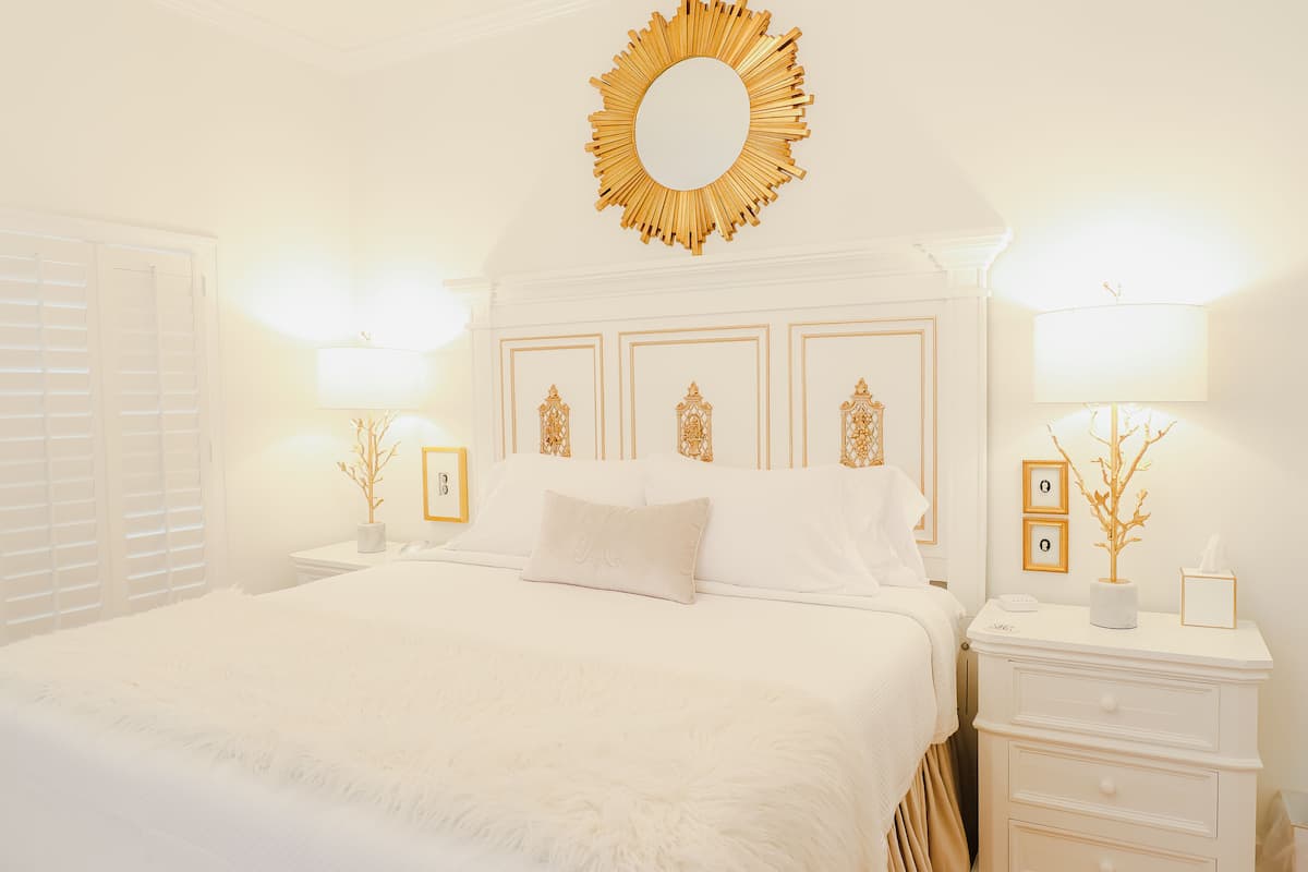 Un dormitorio ordenado con una cama grande, un espejo decorativo y mesitas de noche con lámparas y objetos decorativos.
