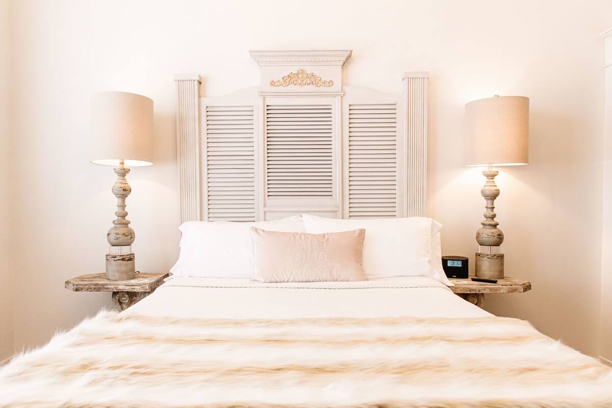 Una cama con un cubreblanco esponjoso, dos mesitas de noche con lámparas, y un adorno en la pared sobre la cama.