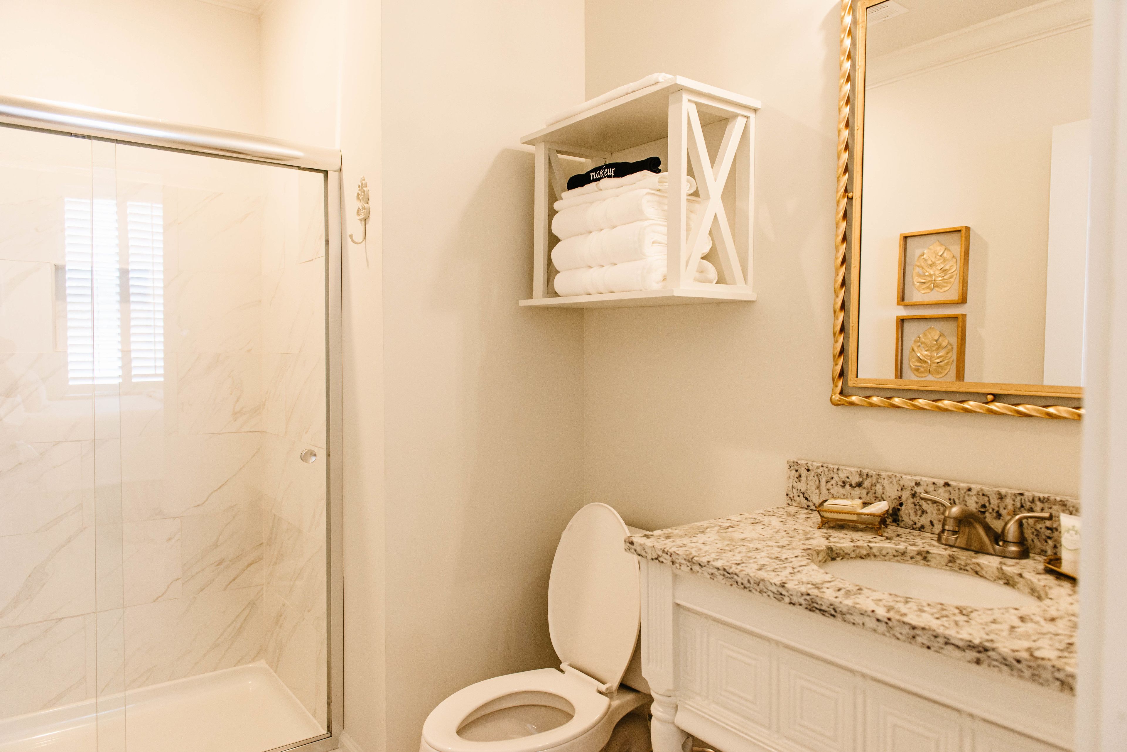 Un baño con ducha envuelta en vidrio, inodoro, lavabo de mármol y toallero blanco con toallas dobladas.