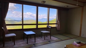 Una habitación con suelo de tatami, una mesa, dos sillas y vistas a un paisaje verde a través de amplios ventanales.