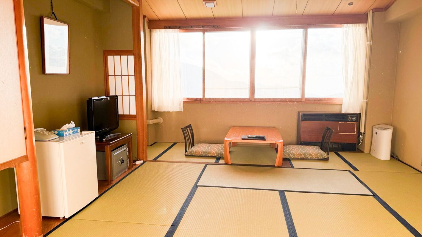 Une pièce de style japonais traditionnel, avec un sol recouvert de tatamis, une petite table basse, un téléviseur et un petit réfrigérateur.