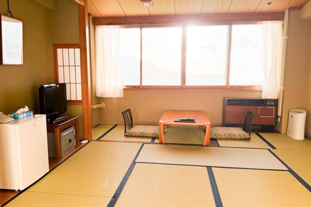 A traditional Japanese room with tatami flooring, a low table, a television, and a small refrigerator.