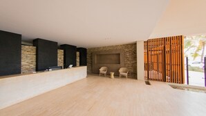 Un'ampia hall con reception in legno, elementi in pietra e vista sull'esterno.