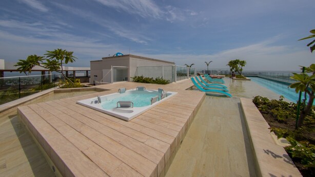 Area piscina sul tetto con vasca idromassaggio, lettini e ringhiera in vetro che si affaccia sull'oceano.