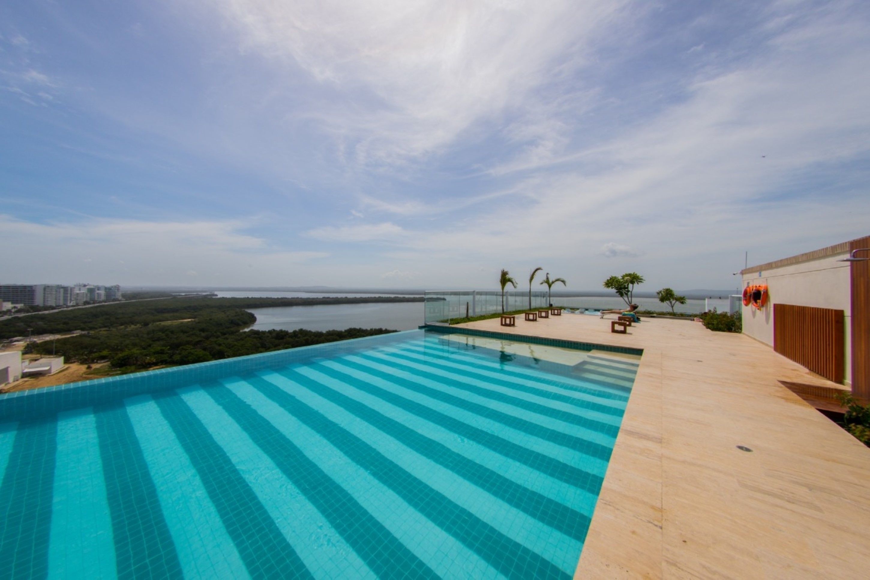 A rooftop infinity pool with a view of the sea and distant cityscape.