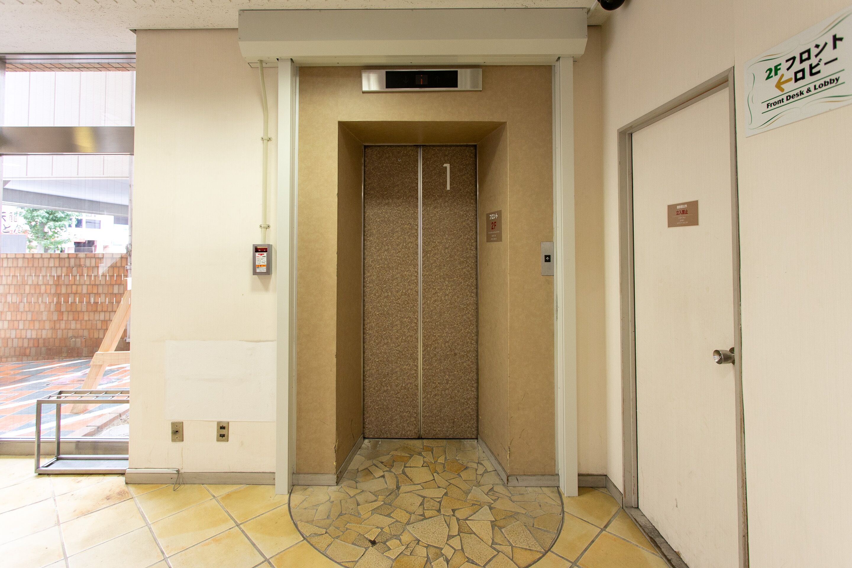 An elevator with a digital display, a tiled floor, and a door with a sign indicating a front desk and lobby.