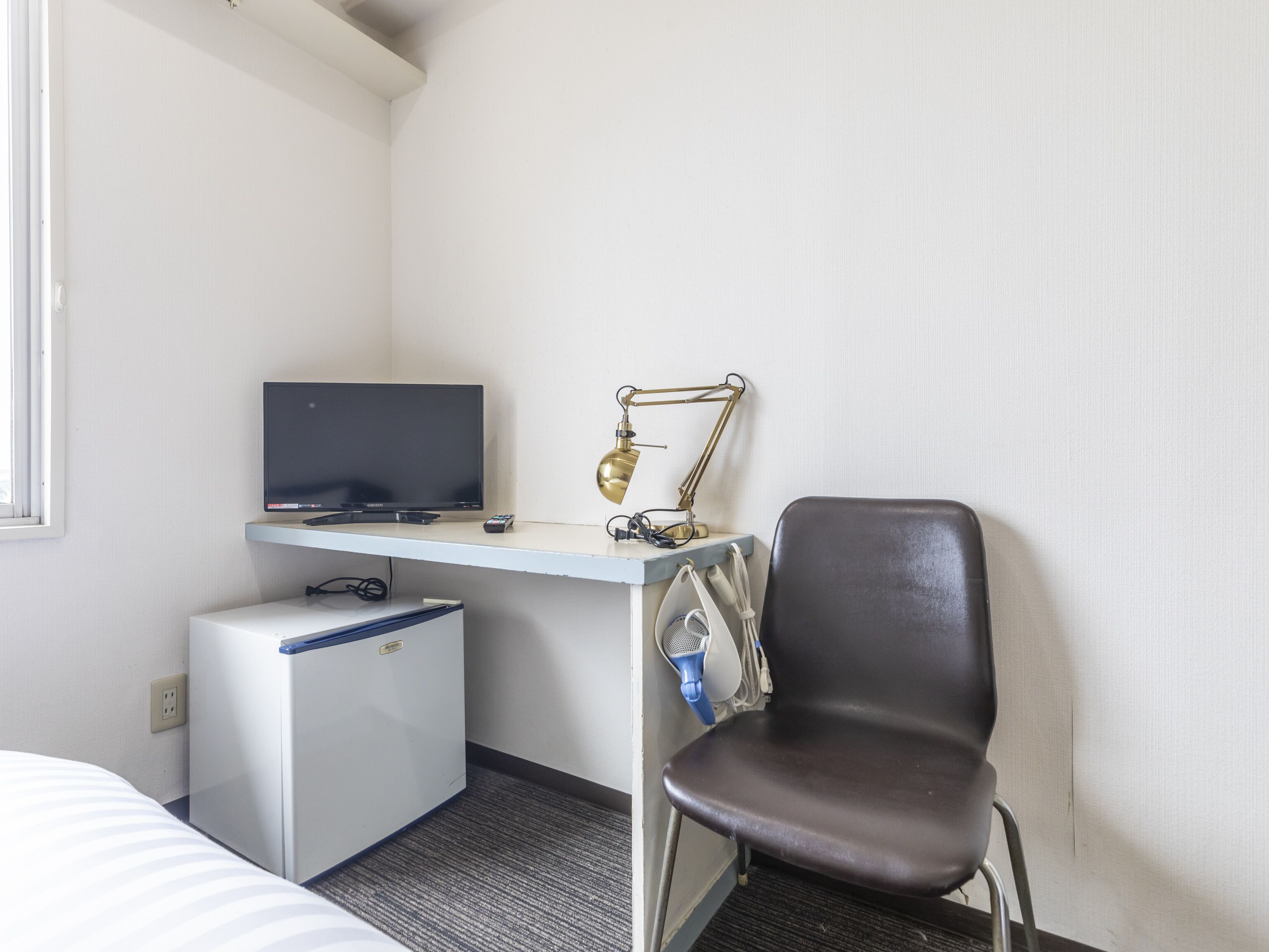 Een hotelkamer met een bed, een bureau met een televisie, een kleine koelkast, een stoel en een bureaulamp.
