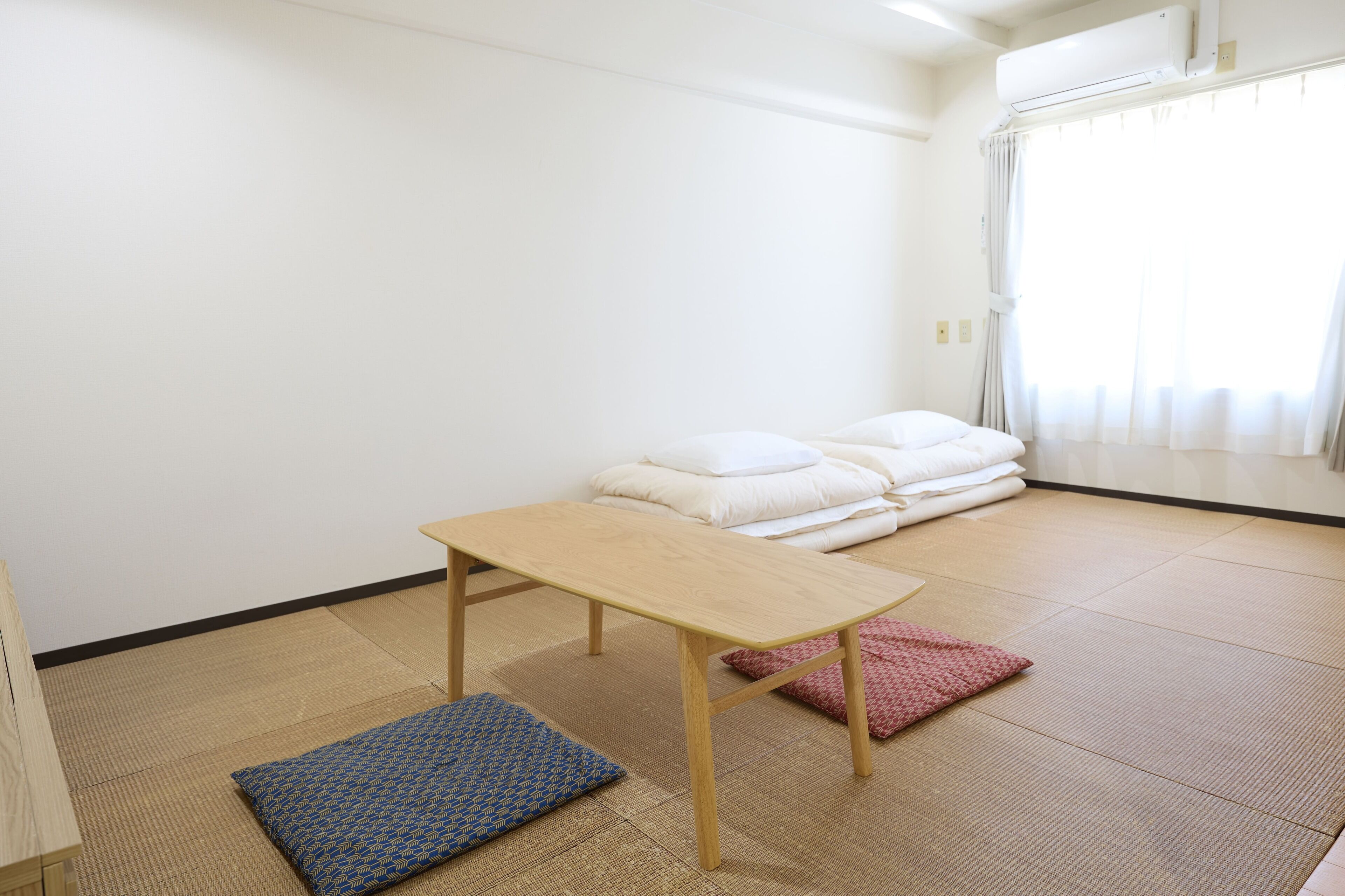 Una habitación con suelo de tatami, una mesa de madera y una cama futón con almohadas.