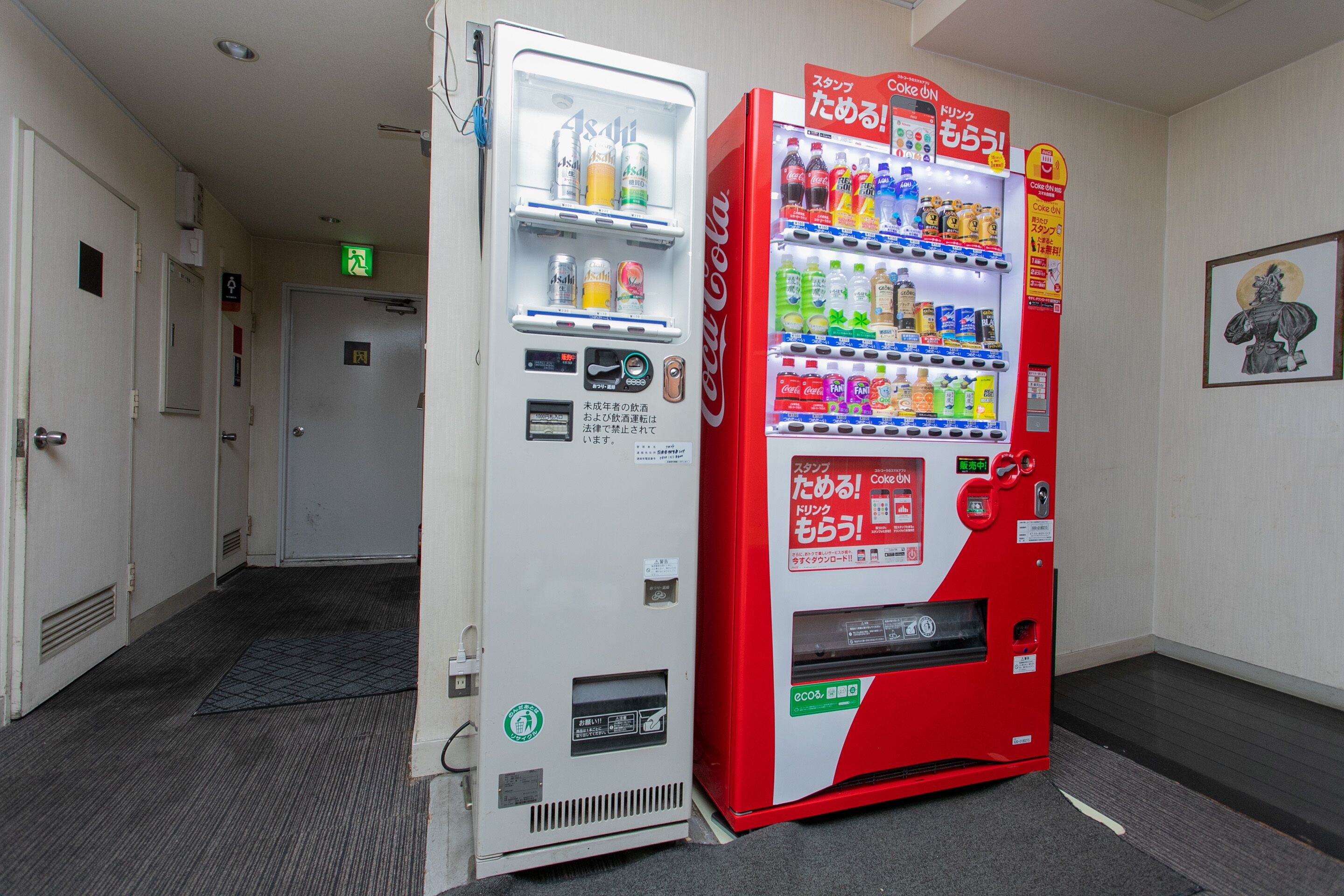 A vending machine with various drinks and snacks, located in a hallway with doors and a carpeted floor.