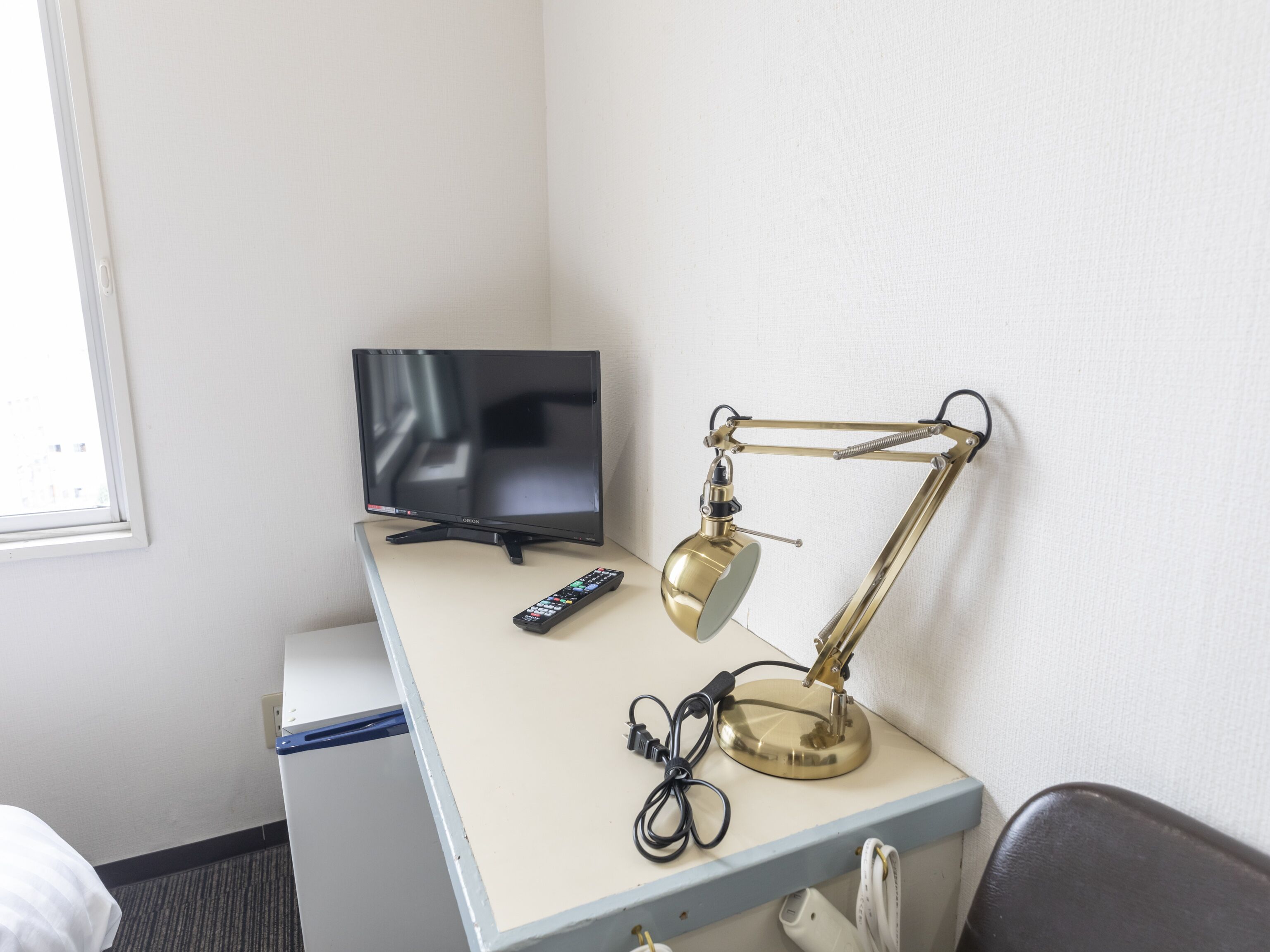 A hotel room with a desk, a television, a desk lamp, and a remote control.