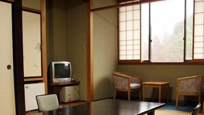 Una habitación japonesa tradicional con suelo de tatami, una mesa baja, sillas, un televisor y un armario.