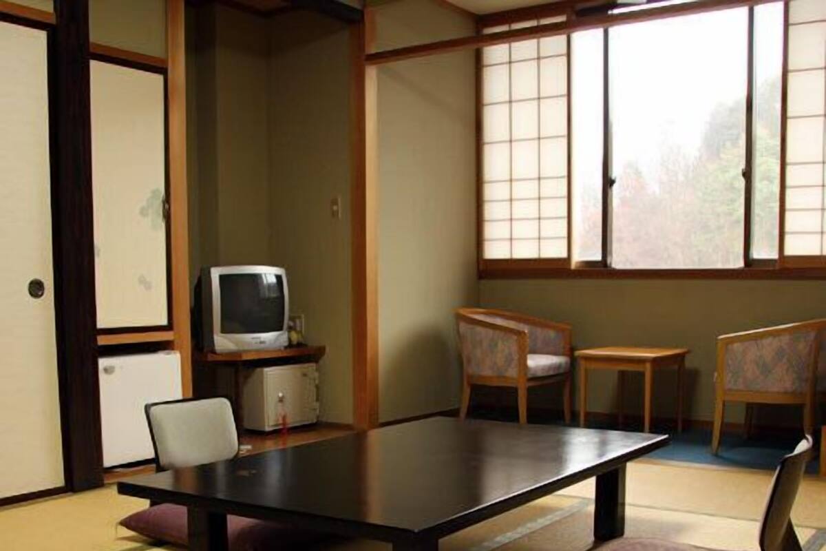 Una habitación japonesa tradicional con suelo de tatami, una mesa baja, sillas, un televisor y un armario.