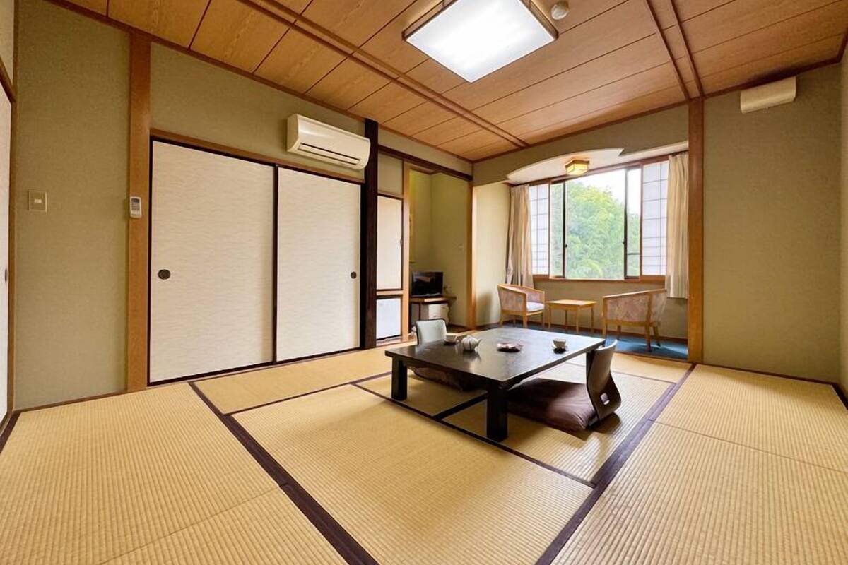 Una habitación con tatamis, una mesa, sillas, puertas correderas y una ventana con vistas.