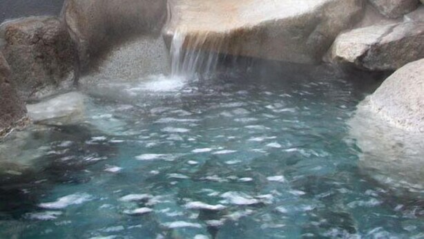 Un manantial termal con agua cristalina, rocas grandes y una cascada.