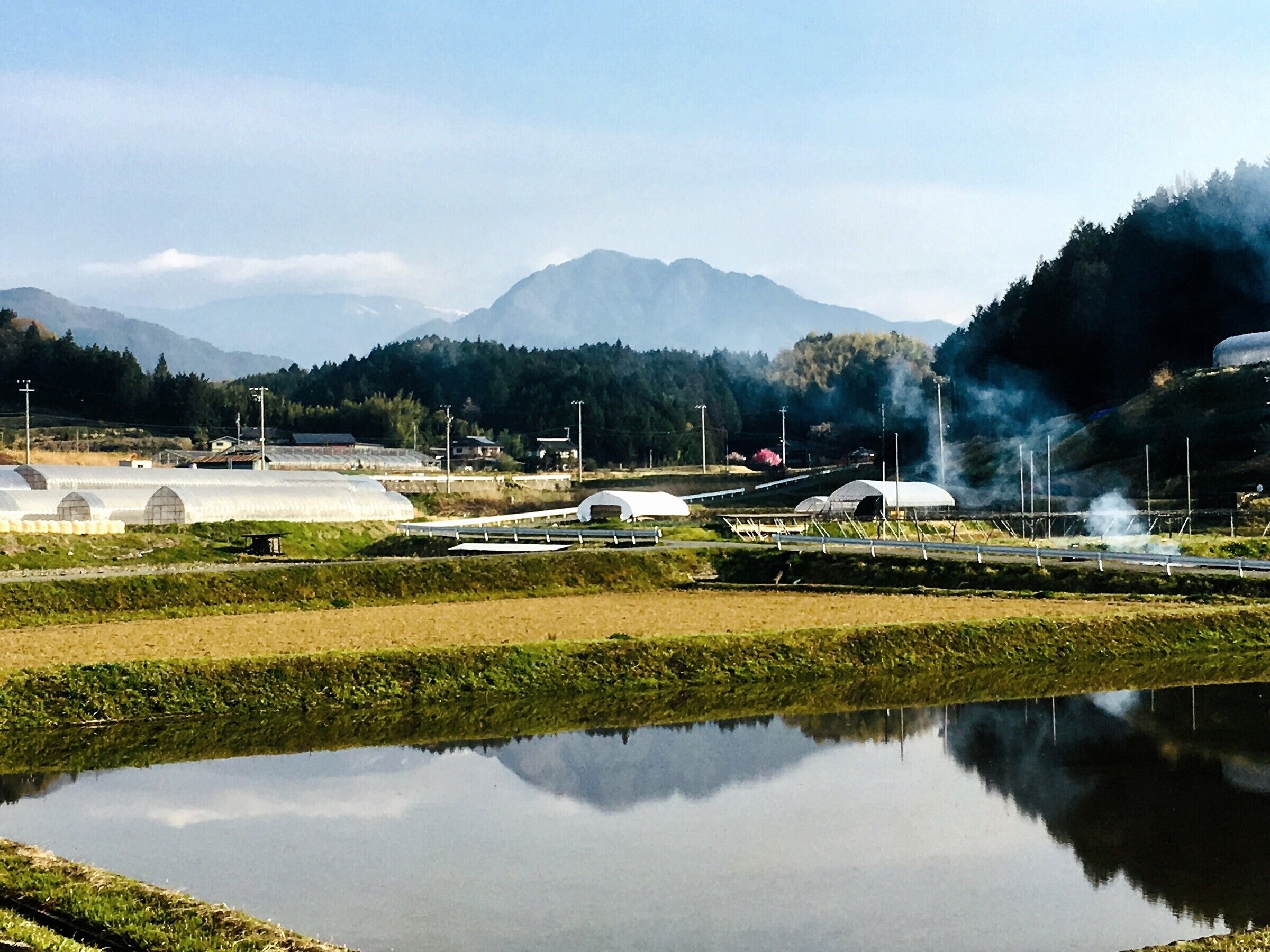 Una instalación tipo invernadero con grandes estructuras blancas en forma de cúpula, una masa de agua tranquila que refleja el entorno y montañas al fondo.