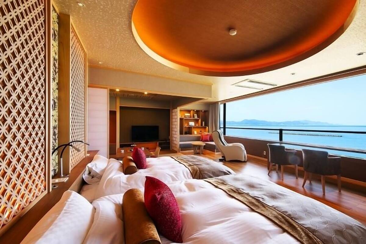 A hotel room with a large bed, a seating area with a TV, and a view of the sea.
