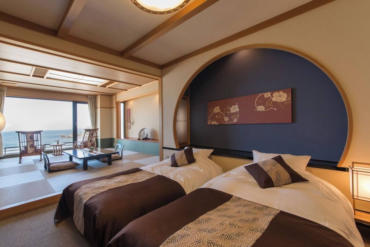 A hotel room with two beds, a sitting area with a view, and a large arched window.
