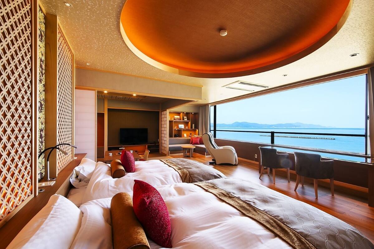 A hotel room with a large bed, a seating area with a TV, and a view of the sea.