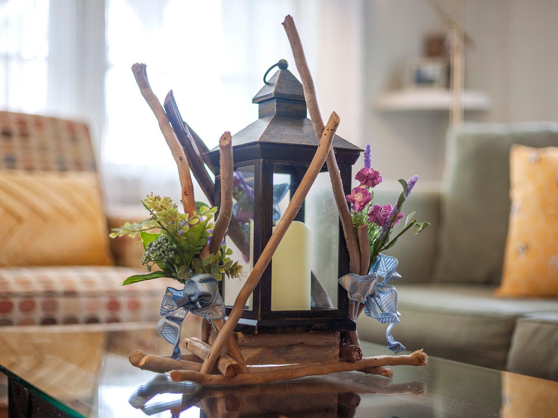 A table with a lantern, two small vases with flowers, and a glass surface reflecting the room.