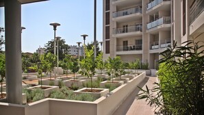 Un edificio moderno con varios balcones y un patio ajardinado con macetas y árboles.