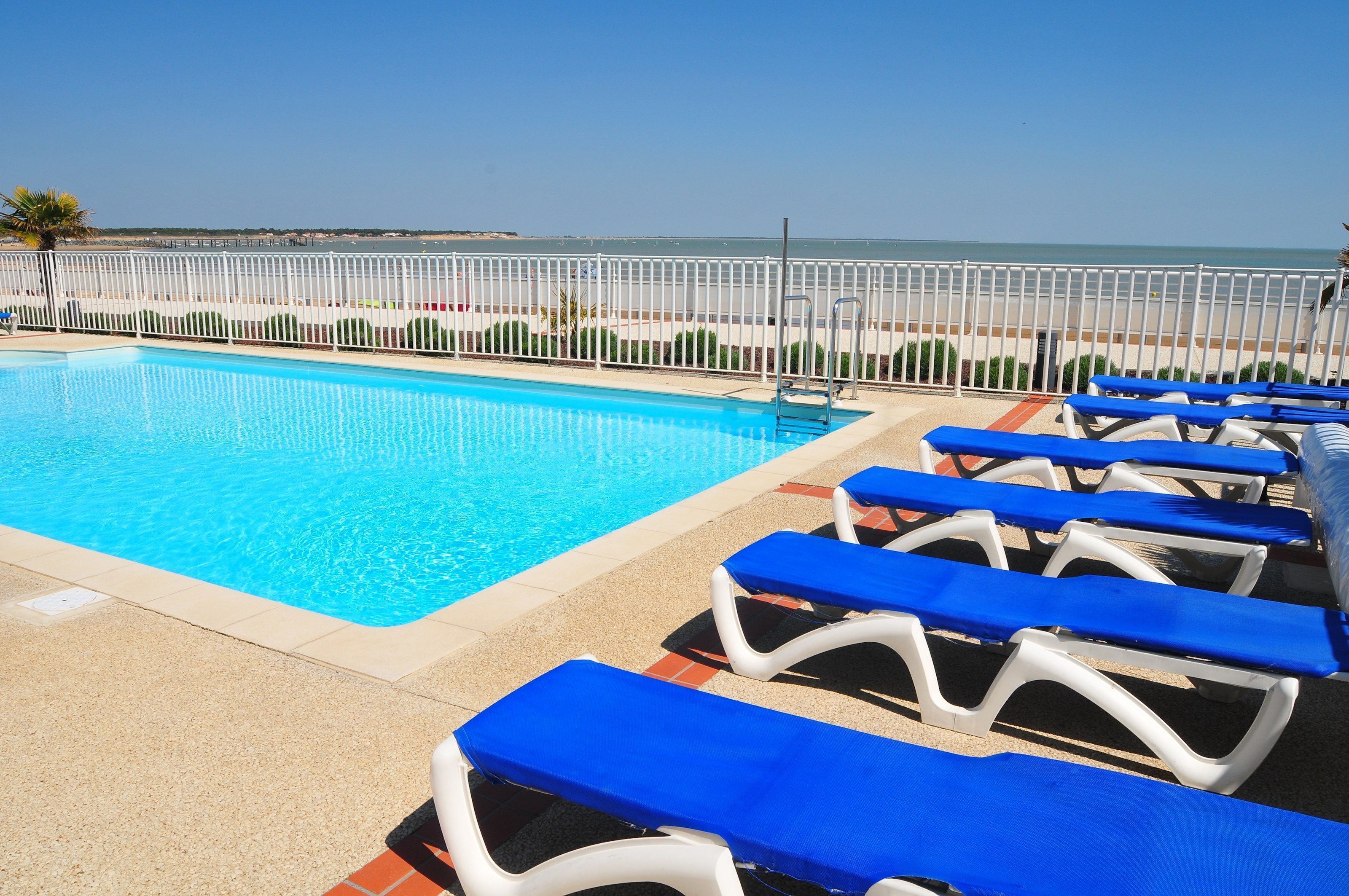 A swimming pool with blue lounge chairs and a view of the beach.