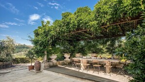 Eine Terrasse im Freien mit einem Steintisch und Stühlen, umgeben von üppigem Grün und einer Pergola.