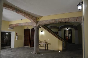 Un pasillo con suelo de piedra, una escalera, un extintor y un banco.