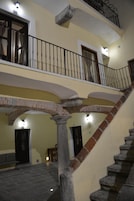 Un interior de varios niveles con una escalera de piedra, varias puertas y un balcón con barandilla de metal.