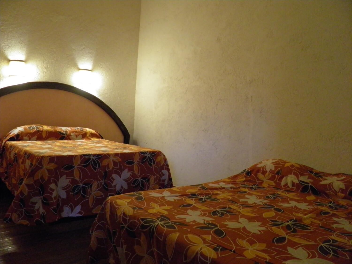 Two single beds with floral-patterned bedding in a room with a plain wall and two wall-mounted lights.