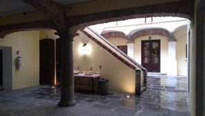 A spacious hallway with a stone floor, a staircase leading to an upper level, and a door at the end. - Hotel Barroco (Puebla)