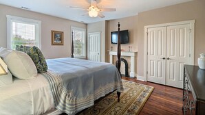 A bedroom with a bed, a ceiling fan, a fireplace, a television, and a set of double doors. - Heated Pool Access | 5*Clean | Flex Cancelation (Savannah)