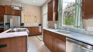 A modern kitchen with wooden cabinets, stainless steel appliances, and a large window offering a view of greenery. - Heated Pool Access | 5*Clean | Flex Cancelation (Savannah)