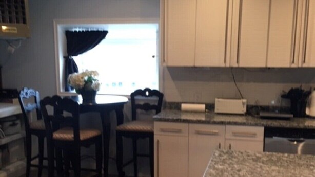 A modern kitchen with white cabinets, a dining table with chairs, and a small island with a sink.
