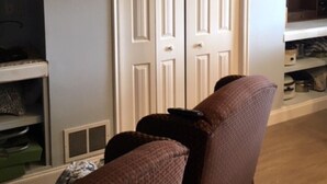 A room with a wooden floor, a brown sofa, a white wardrobe, and a wall clock.