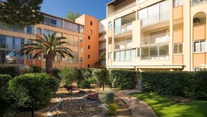 Un immeuble résidentiel à plusieurs étages, doté de balcons, d’un jardin avec des palmiers et d’un chemin en pierre.