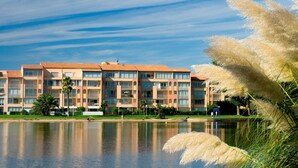 Un hôtel à plusieurs étages doté de balcons, situé en bordure d’un lac, avec un ciel dégagé.