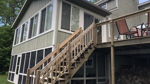 Een huis met twee verdiepingen en een houten trap die uitkomt op een overdekt terras.