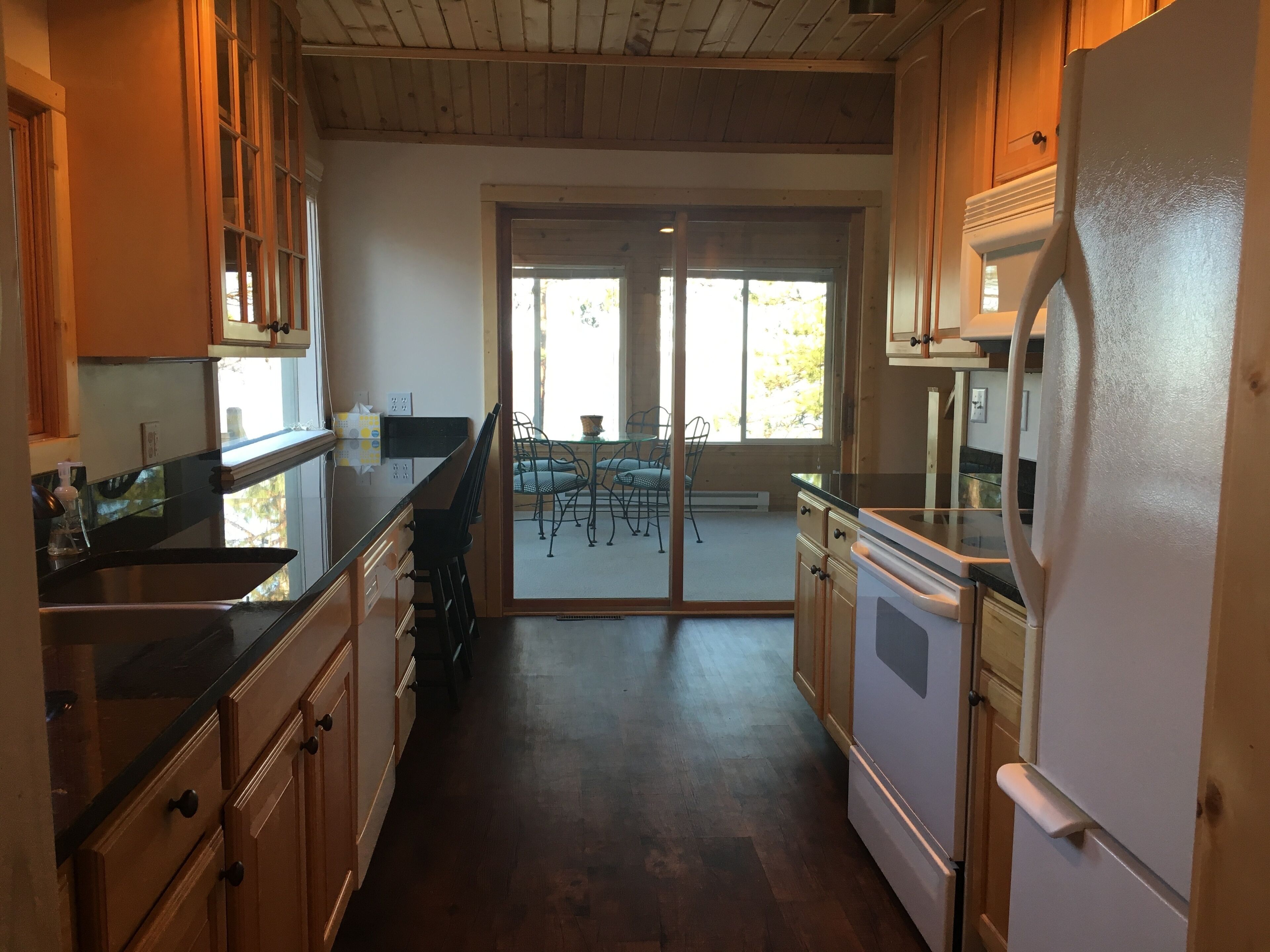 A kitchen with wooden cabinets, a stainless steel sink, and a refrigerator. There is a sliding glass door leading to a patio area with outdoor furniture.