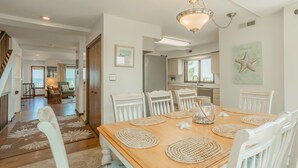 Un comedor con una mesa de madera, sillas blancas y individuales tejidas.