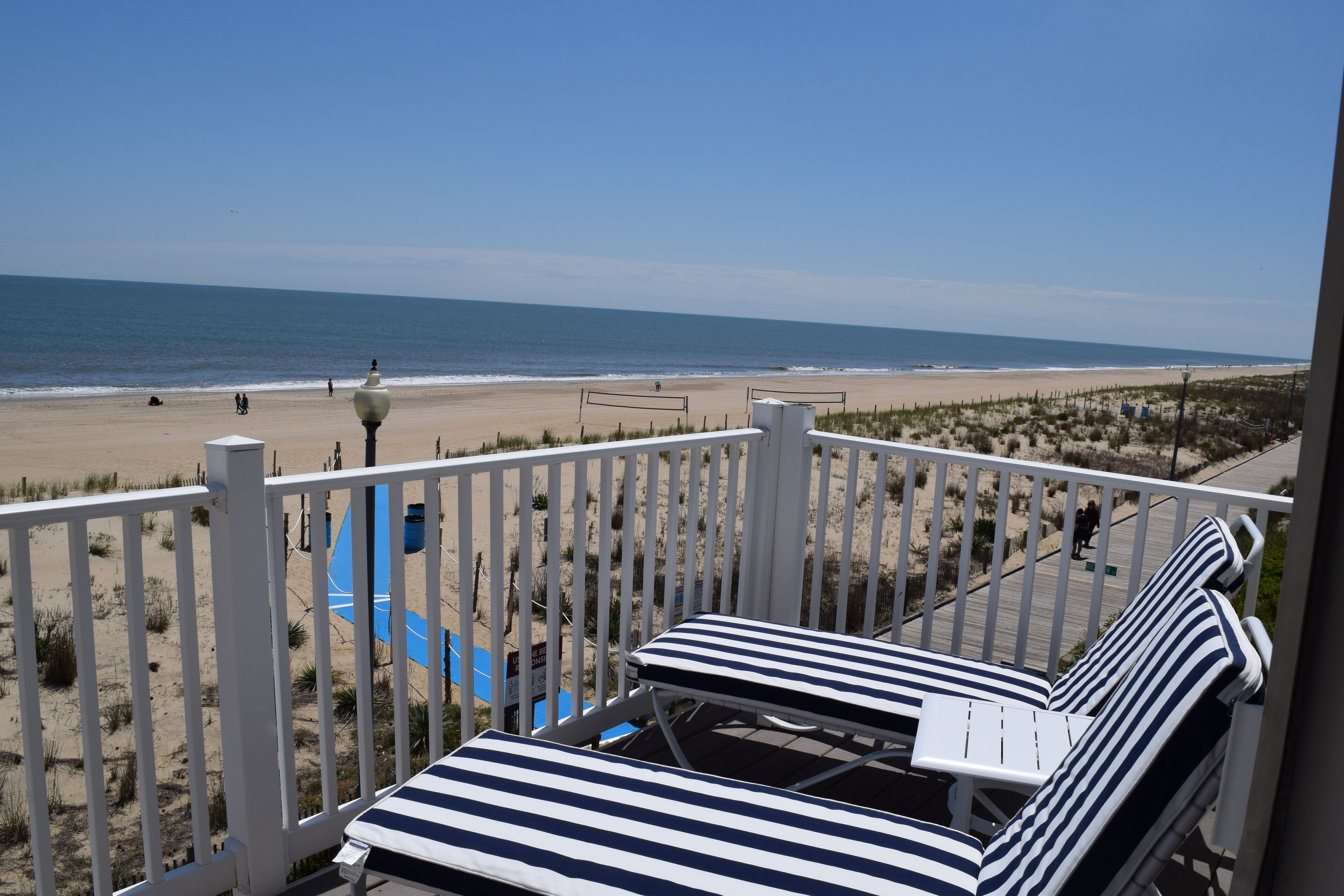 Een balkon met gestreepte lounge fauteuils met uitzicht op een strand.
